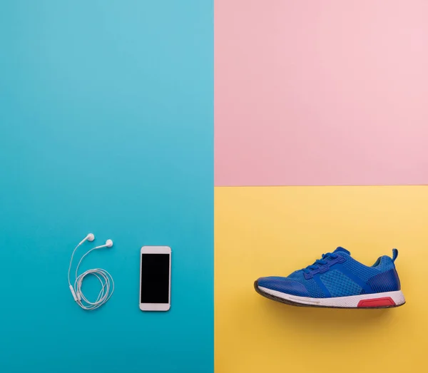 Una toma de estudio de zapatillas y teléfonos inteligentes en el fondo de color. Puesta plana . —  Fotos de Stock