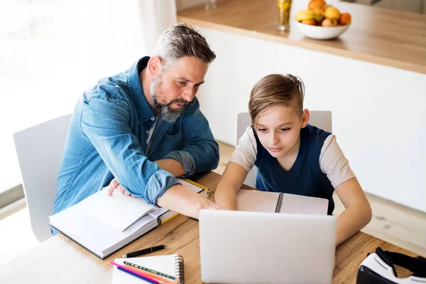 Dojrzały ojciec z małym synem siedzi przy stole w pomieszczeniu, za pomocą laptopa. — Zdjęcie stockowe