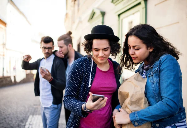 Um grupo de jovens amigos com smartphone em pé ao ar livre na cidade, conversando . — Fotografia de Stock