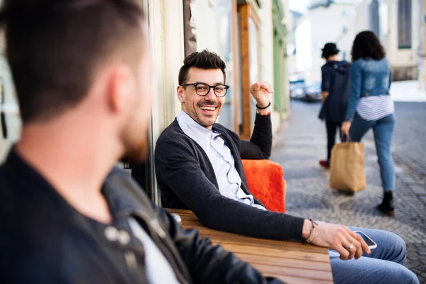 Jóvenes amigos con smartphone sentados en un café al aire libre, hablando . —  Fotos de Stock