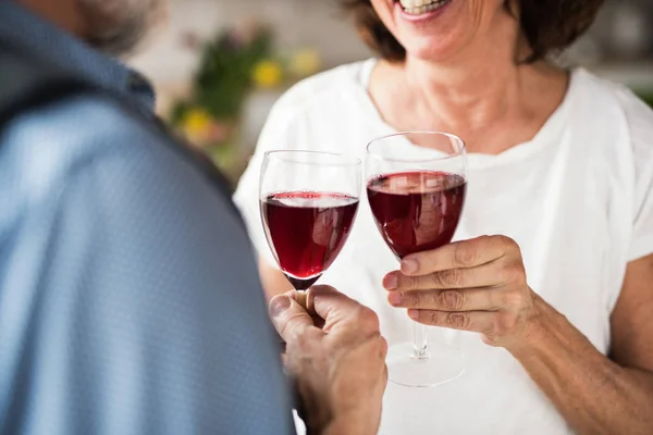 Una sección media de la pareja de ancianos enamorados en el interior de casa, tintineo de vino . — Foto de Stock