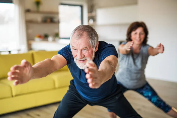 Una coppia di anziani al chiuso a casa, facendo esercizio al chiuso . — Foto Stock