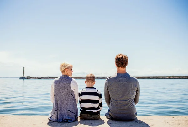 Rückansicht einer jungen Familie mit Sohn, die auf einem Pier in Conrete am Meer sitzt. — Stockfoto