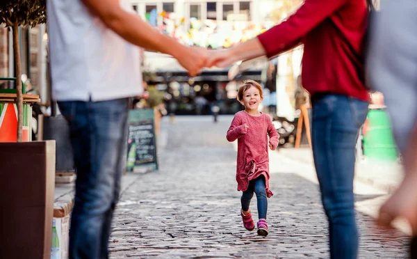 Egy kicsi lány futás felé felismerhetetlen szülők kint a városban. — Stock Fotó