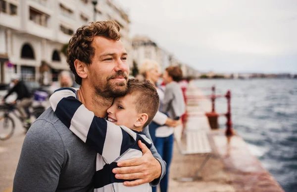 Padre con hijo pequeño parado al aire libre en la ciudad junto al mar, abrazando . — Foto de Stock