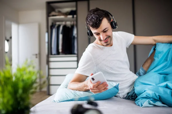 Giovane con cuffie e smartphone a letto a casa, ascoltando musica . — Foto Stock