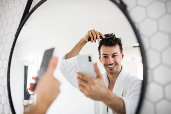 Junger Mann kämmt morgens im Badezimmer die Haare und macht ein Selfie. — Stockfoto