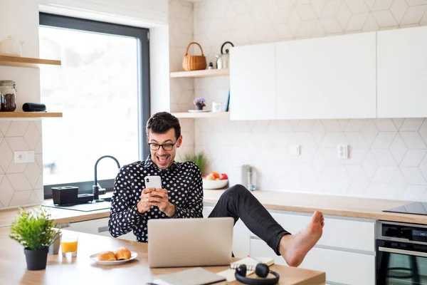 Jovem com smartphone e laptop, tomando café da manhã em casa . — Fotografia de Stock