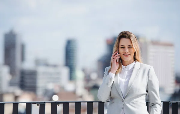 Eine junge Geschäftsfrau mit Smartphone steht auf einer Terrasse und arbeitet. — Stockfoto