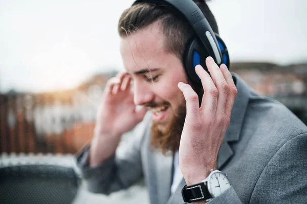 Un jeune homme d'affaires avec écouteurs sur une terrasse, écoutant de la musique . — Photo