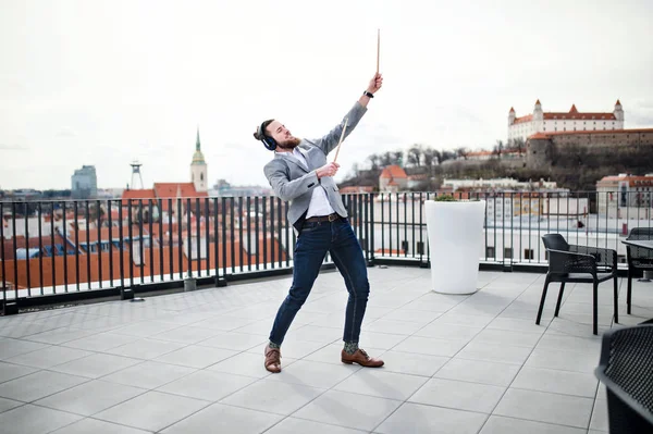 Ein junger Geschäftsmann mit Kopfhörern steht auf einer Terrasse und hat Spaß. — Stockfoto