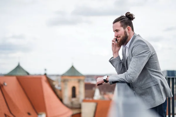 Un jeune homme d'affaires avec smartphone debout sur une terrasse, faisant un appel téléphonique . — Photo