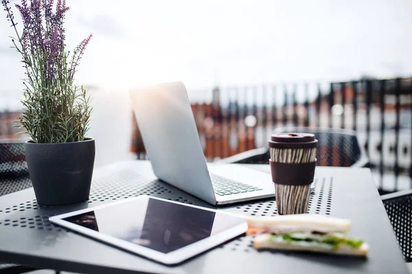 Laptop, tablet, sanduíche e café em uma mesa em um terraço fora do escritório . — Fotografia de Stock