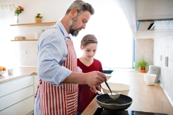 Mogen far med liten son inomhus i köket, gör pannkakor. — Stockfoto