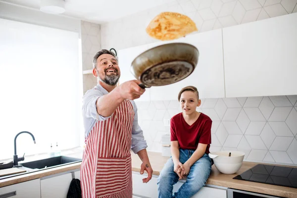 Mogen far med liten son inomhus i köket, vända pannkakor. — Stockfoto