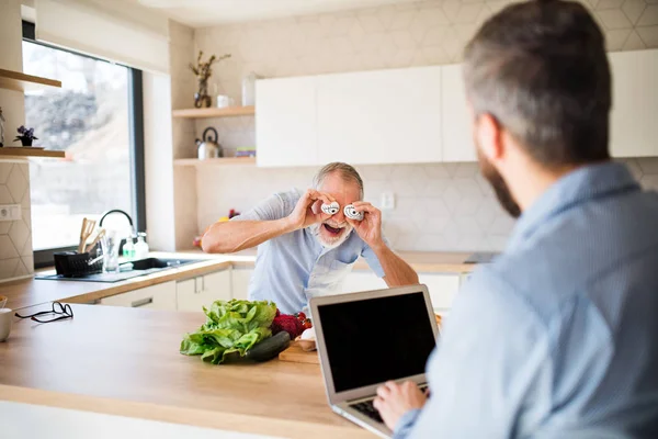 Adulte hipster fils et père aîné à l'intérieur dans la cuisine à la maison, en s'amusant . — Photo