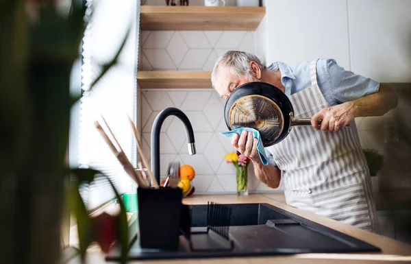 En senior man inomhus i köket hemma, tvätta upp en kastrull. — Stockfoto