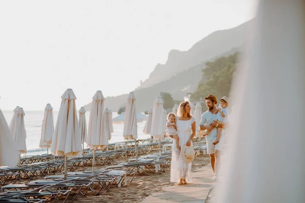 Una familia joven con dos niños pequeños caminando en la playa en vacaciones de verano . —  Fotos de Stock