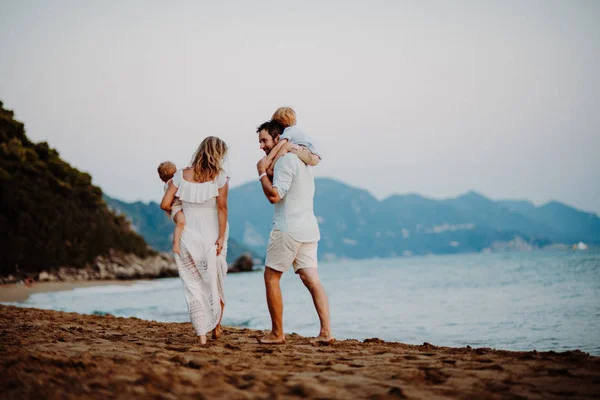 Vista trasera de la familia con dos niños pequeños caminando en la playa en vacaciones de verano . — Foto de Stock