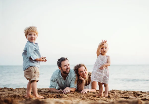 Egy család, két totyogó fekvő homokos strand, a nyári szünet. — Stock Fotó