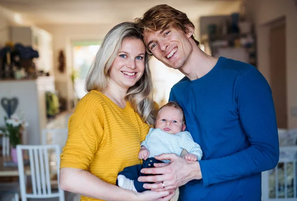Front view portrait of beautiful young parents with a newborn baby at home. — Stock Photo, Image