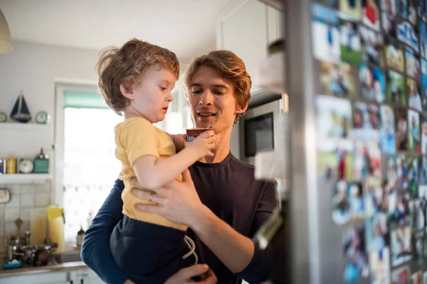 A happy father with a toddler son indoors in kitchen at home.