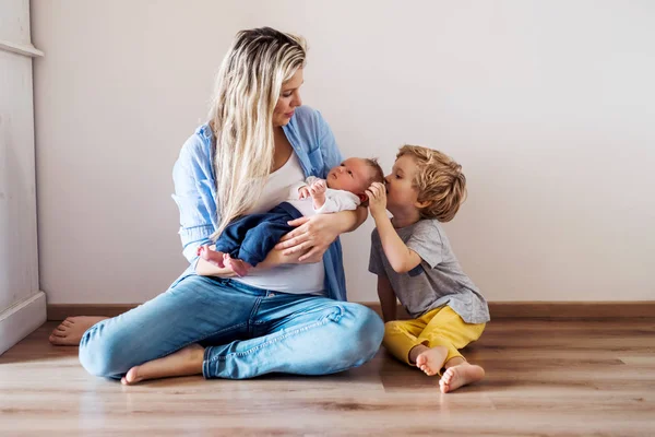 Uma bela jovem mãe com um bebê recém-nascido e seu irmão em casa . — Fotografia de Stock