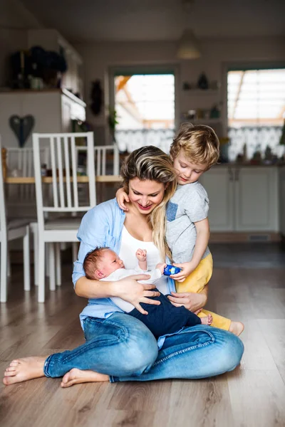 A beautiful young mother with a newborn baby and his brother at home. — Stock Photo, Image