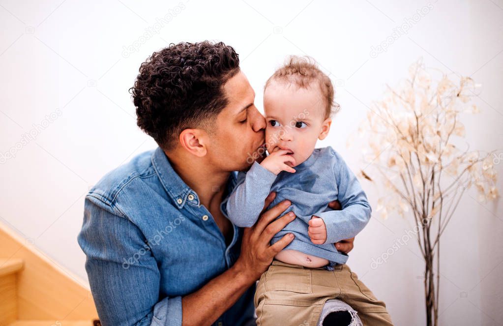 A portrait of father and small toddler son indoors at home, sitting on staircase.