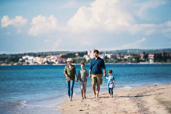 Junge Familie mit zwei kleinen Kindern geht draußen am Strand spazieren. — Stockfoto