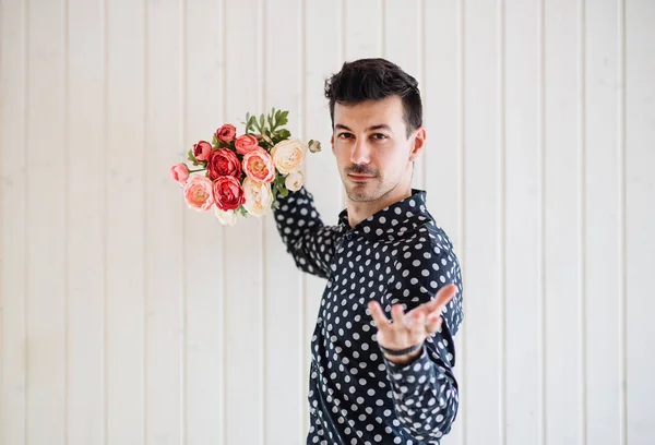 Beyaz ahşap arka plan duvarına karşı duran çiçekleri olan genç adam. — Stok fotoğraf