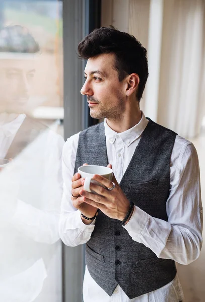 Young man with coffee standing by the window. Copy space. — Stock Photo, Image