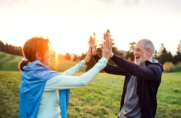 An active senior couple resting after doing exercise in nature at sunset. — Stock Photo, Image