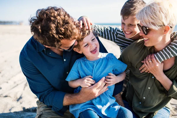 Junge Familie mit zwei kleinen Kindern sitzt draußen am Strand und hat Spaß. — Stockfoto