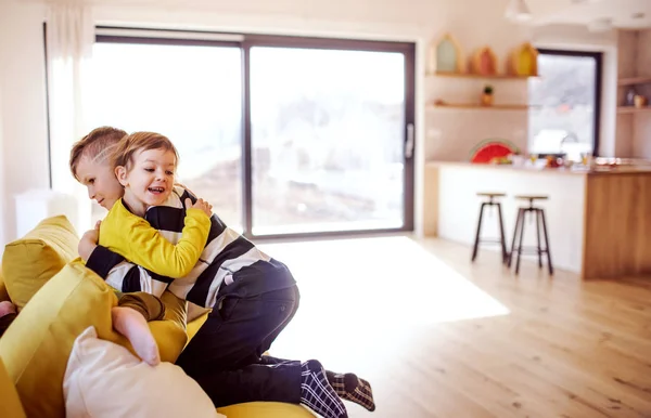 Två glada barn sitter på soffan inomhus hemma, kramas. — Stockfoto