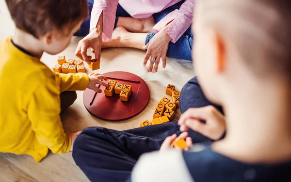 Una sección media de la madre con dos niños jugando juegos de mesa en el suelo . — Foto de Stock