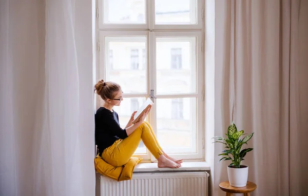 Młoda studentka z książką siedzącą na parapecie, studiując. — Zdjęcie stockowe