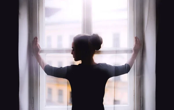 Rückansicht einer jungen, traurigen Studentin, die am Fenster steht. — Stockfoto