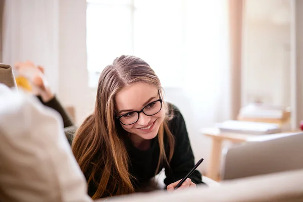 O tânără studentă întinsă pe canapea, studiind . — Fotografie, imagine de stoc