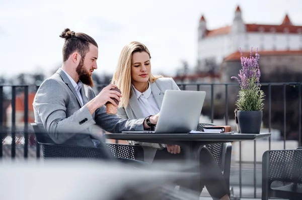 Zwei junge Geschäftsleute mit Laptop sitzen auf einer Terrasse vor dem Büro und arbeiten. — Stockfoto