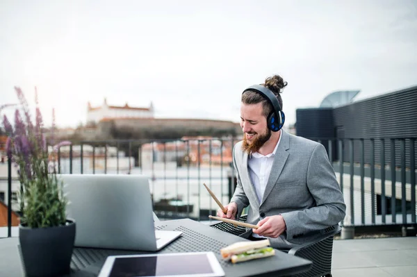 Un jeune homme d'affaires avec écouteurs assis sur une terrasse, s'amuser . — Photo