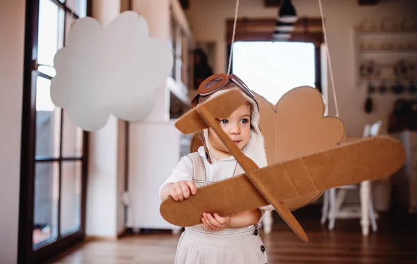 Una niña pequeña con avión de cartón jugando en casa, concepto de vuelo . — Foto de Stock