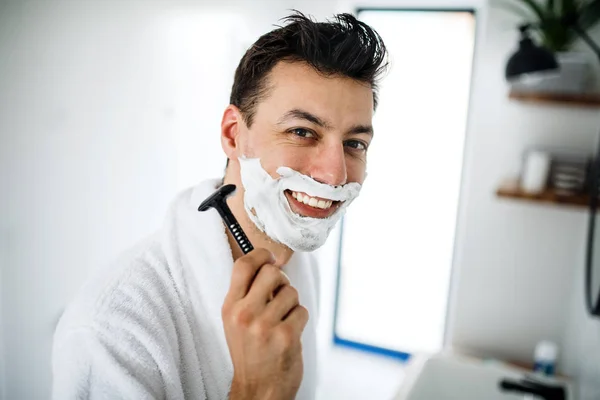 Young man with shaving foam in the bathroom in the morning, daily routine. — Stock Photo, Image