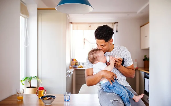 Un biberón paterno alimentando a un pequeño hijo en casa . — Foto de Stock