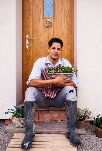 Portret młodego człowieka ogrodnika siedzącego przed drzwiami w domu. — Zdjęcie stockowe