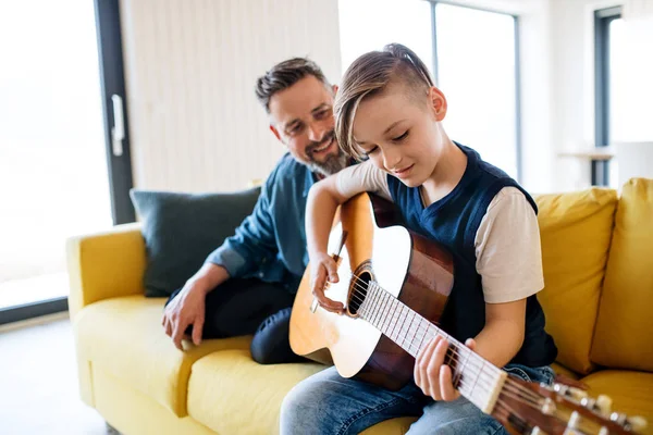 Küçük oğlu ile olgun baba kanepede kapalı oturan, gitar çalıyor. — Stok fotoğraf