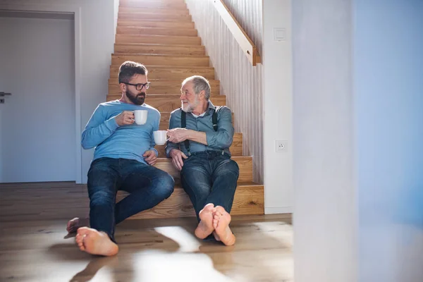 집에서 실내 계단에 앉아 있는 성인 힙스터 아들과 선배 아버지가 이야기하고 있습니다.. — 스톡 사진