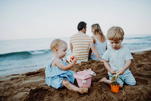 Bambini piccoli con i genitori che giocano sulla spiaggia di sabbia in vacanza estiva . — Foto Stock
