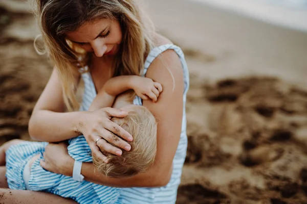 Joven madre amamantando a su hija en la playa en vacaciones de verano . — Foto de Stock