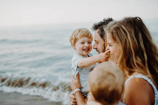 Una familia joven con dos niños pequeños de pie en la playa en las vacaciones de verano . —  Fotos de Stock